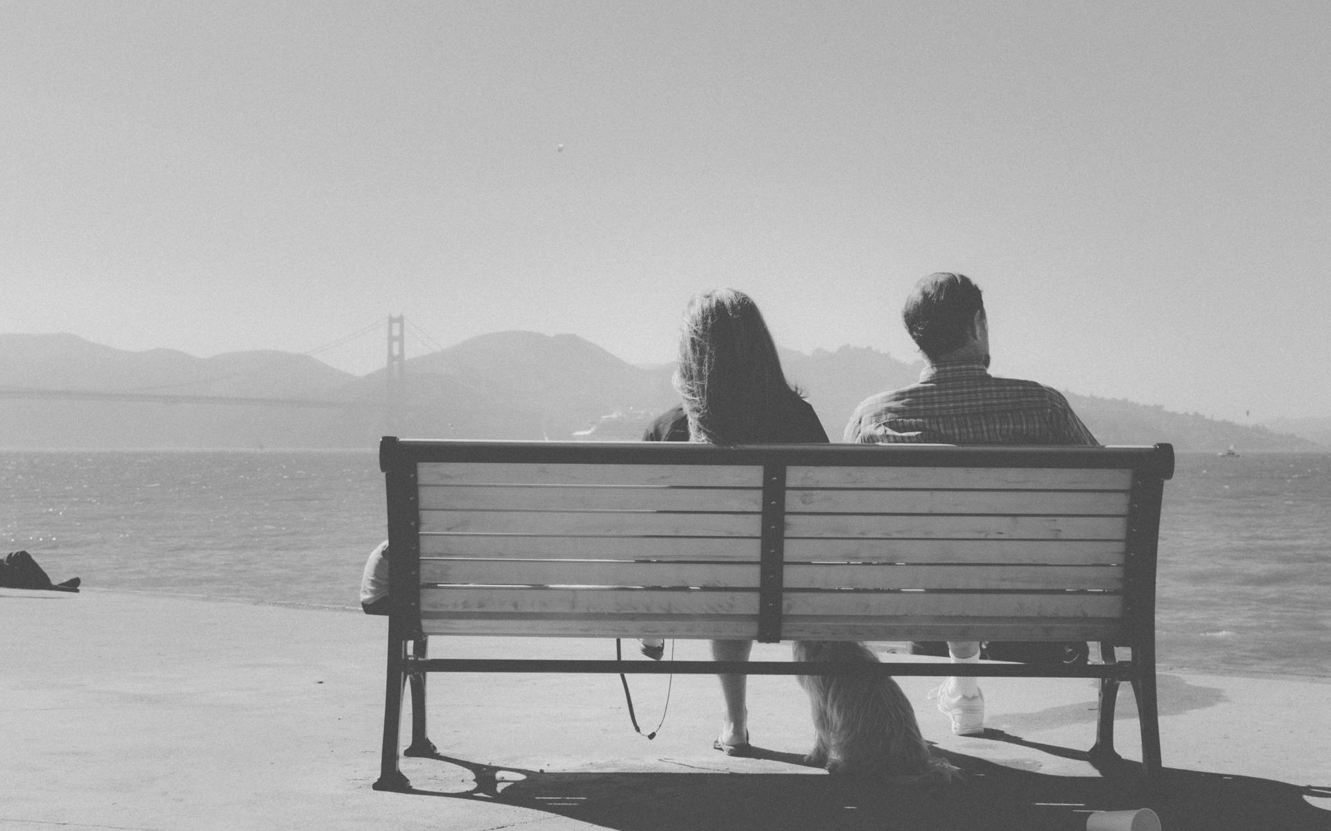 A guy and a girl sitting together on a bench overlooking the water